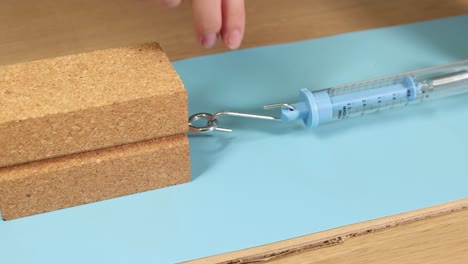 a hand uses a spring scale to measure friction on a wooden block. bright lighting and close-up focus enhance the experiment