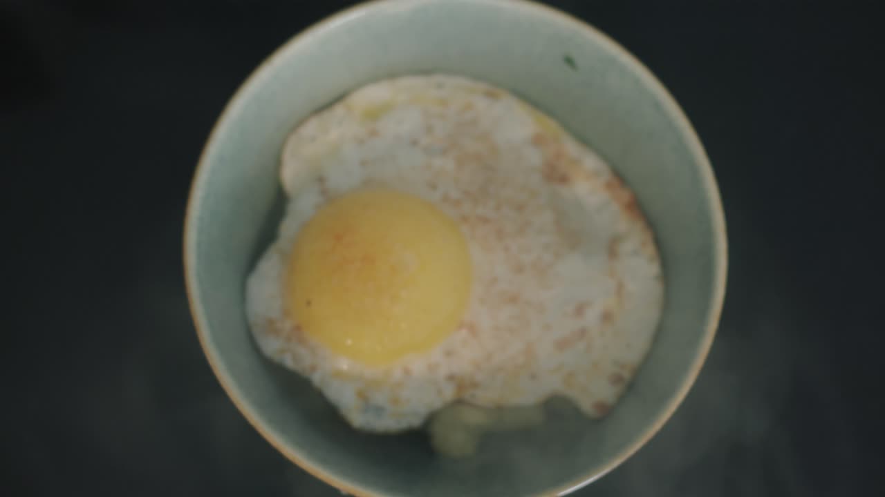 egg being placed over cauliflower vegetarian meal on black marble kitchen-top in sea green bowl