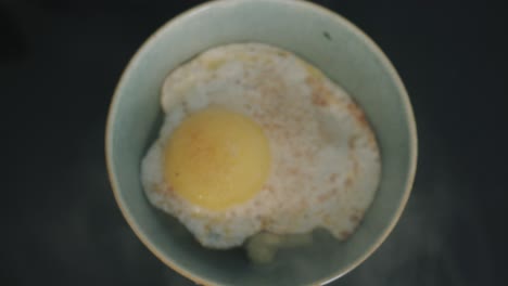 egg being placed over cauliflower vegetarian meal on black marble kitchen-top in sea green bowl
