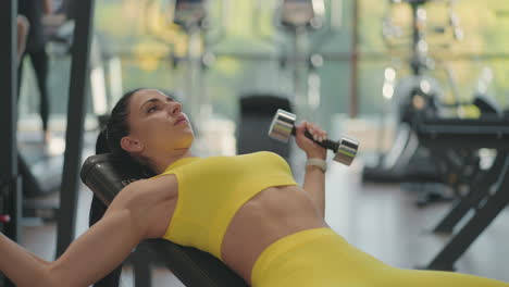 Una-Hermosa-Mujer-Atlética-Entrena-Los-Músculos-Pectorales-Criando-Pesas-Mientras-Está-Acostada-En-El-Gimnasio.-Entrenamiento-De-Atleta-Musculosa-Con-Pesas-Levantando-Pesas