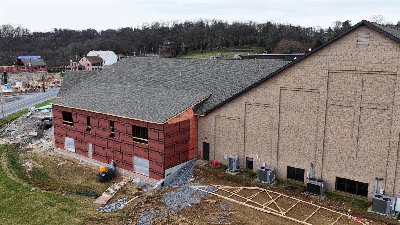 Aerial view of church building under construction in Pennsylvania, with brick exterior walls, large cross on facade and surrounding construction site in suburban American neighborhood of Lancaster.