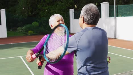 video of happy biracial senior couple embracing after after match on tennis court