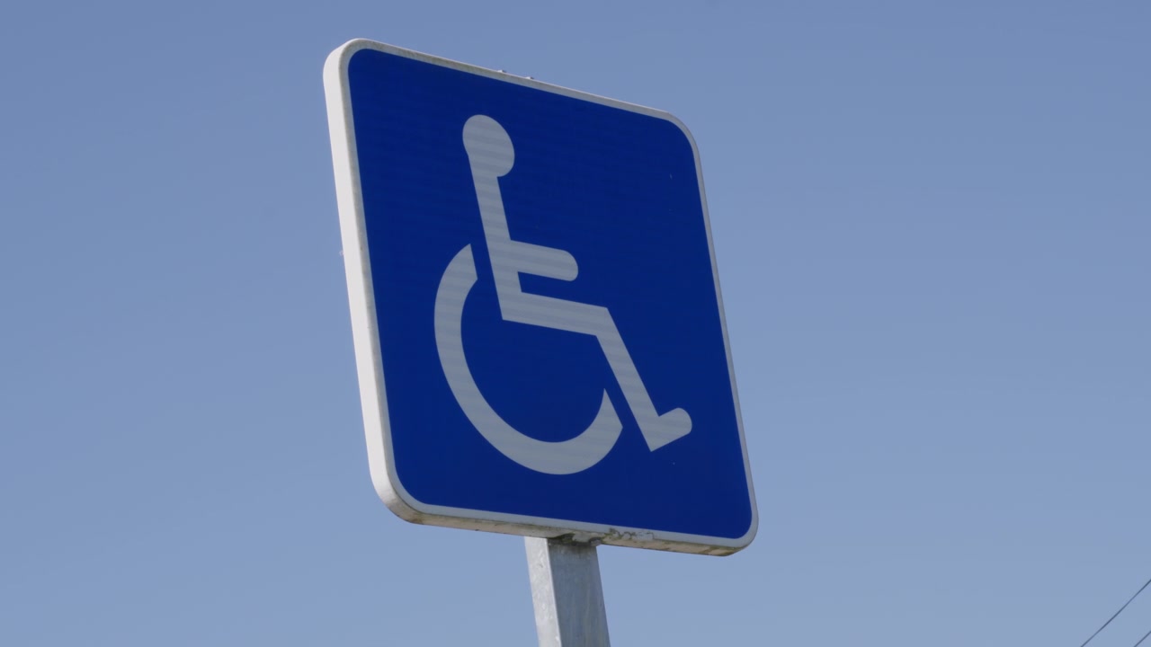 Close-up em ângulo baixo de uma placa azul de estacionamento para pessoas com deficiência, fotografada à luz do dia com céu limpo. Composição nítida e estática, ideal para temas de acessibilidade