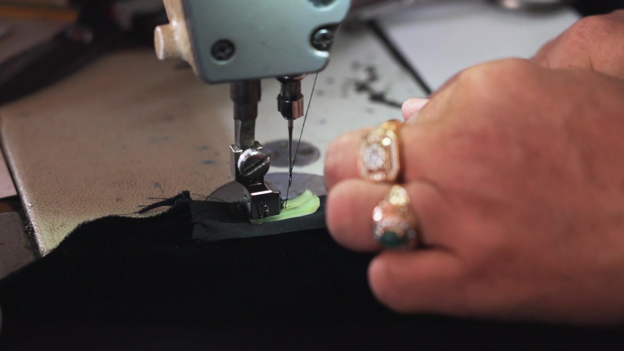 Slow Motion close-up of a sewing machine stitching fabric for a traditional songkok in Malaysia. Skilled craftsmanship and precise hand guidance highlight cultural garment production.