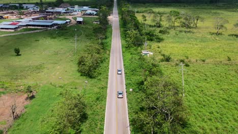 Amplia-Panorámica-Aérea-De-Los-Coches-Que-Viajan-Por-Un-Largo-Camino-Sin-Fin-A-Través-De-Exuberantes-Campos-Verdes-En-Un-Día-Soleado-De-Verano