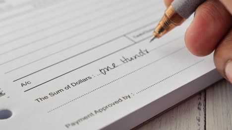 close-up of a hand writing a check for one hundred dollars