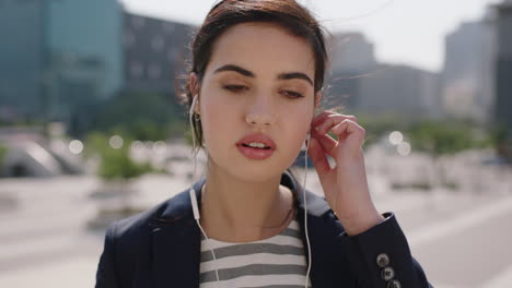 retrato en primer plano de una hermosa mujer de oriente medio sonriendo pasante feliz escuchando música usando auriculares disfrutando de un día soleado y ventoso en el fondo de la ciudad urbana
