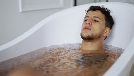 man sits with closed eyes in the bath with ice cubes for recovery