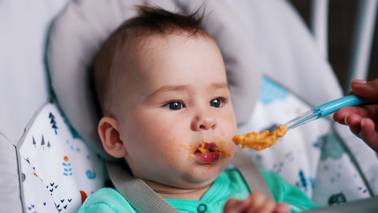 Baby making dramatic face while he is being fed. Mom shoves the full spoon to son's mouth close up.