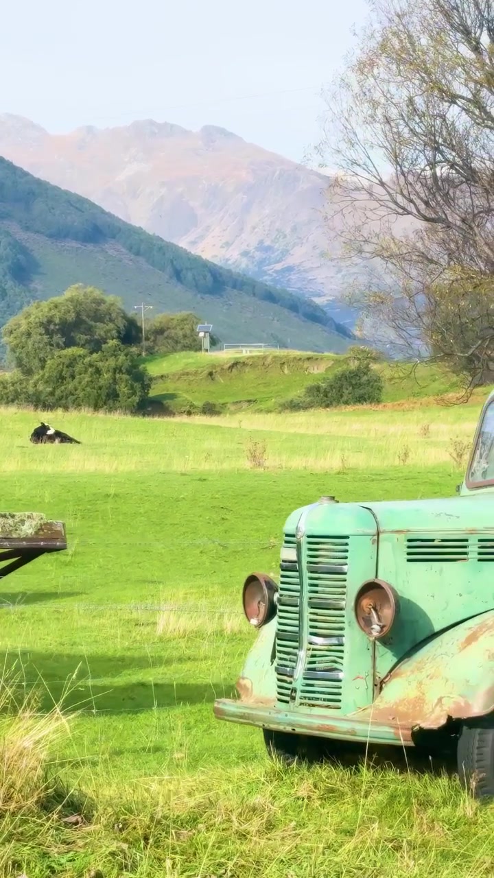 Ein Oldtimer-LKW auf einem üppig grünen Feld mit Bergen, bei hellem Tageslicht, der eine friedliche ländliche Szene schafft