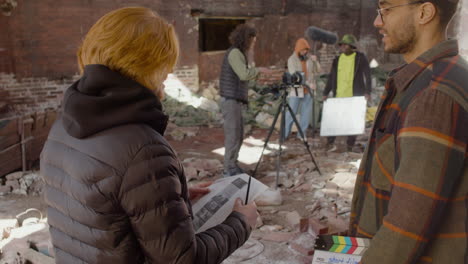 close up view of two production coworkers talking and reading a document about the movie in a ruined building while other colleagues preparing for the recording