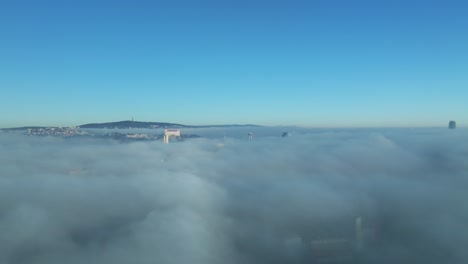 captivating aerial journey with a drone moving forward, capturing bratislava's castle and buildings emerging through thick inversion clouds