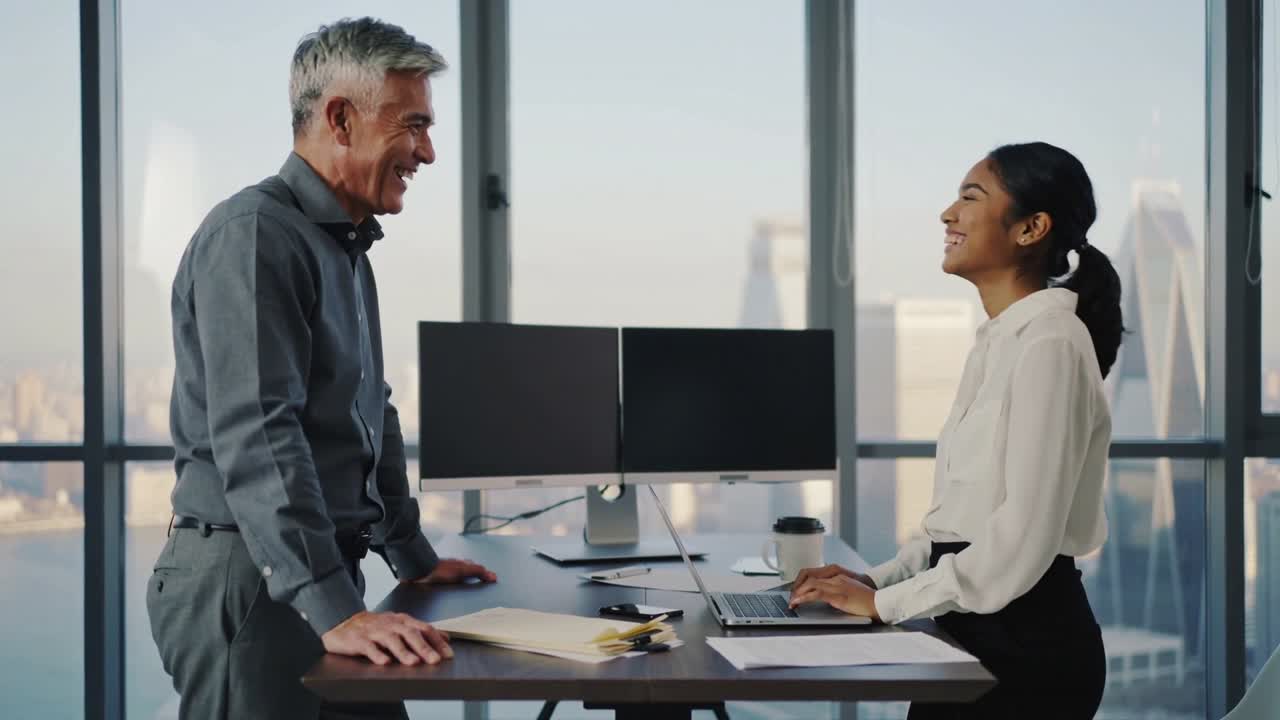 Making eye contact, coworkers in workwear leaning and typing at laptop, laughing for work in office