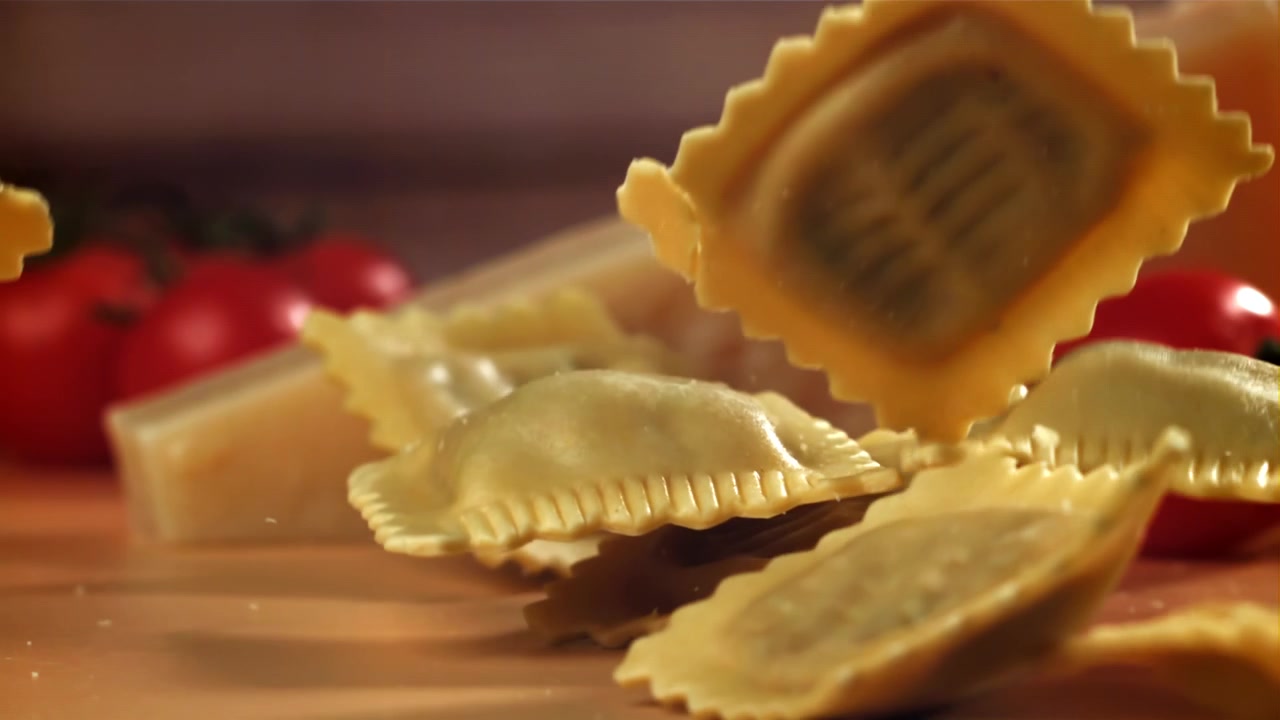 Zpomalený záběr na čerstvé ravioli padající na stůl se sýrem a rajčaty