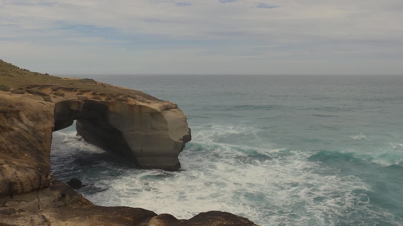 olas rompiendo dentro de un increíble arco de roca natural - vía de la playa del túnel, dunedin