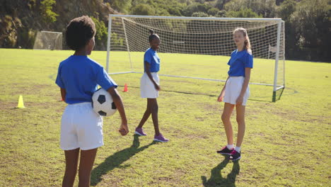 playing soccer on school field, three girls in sports uniforms with soccer ball