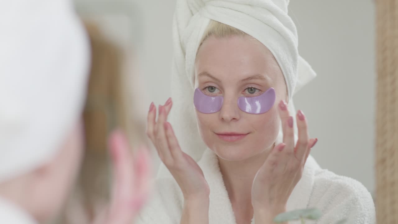 행복하고 매력적인 여성은 화장실 거울을 바라보는 눈 관리 패치를 적용합니다. 건강하고 아름답고 성숙한 여성은 눈 아래에 얼굴 피부 관리 보습 패드를 넣습니다.