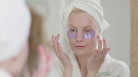 feliz mujer atractiva aplicar parches de cuidado de los ojos mirando en el espejo del baño, saludable hermosa dama adulta poner debajo de los ojos cuidado de la piel de la cara almohadillas hidratantes