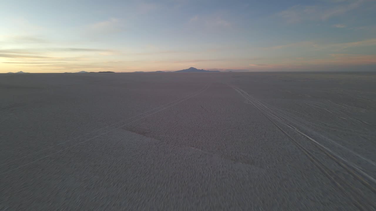 Seseorang bergerak melintasi permukaan Uyuni yang tergenang air dan memantulkan cahaya saat pagi hari dengan cahaya keemasan.