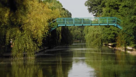 toma manual en cámara lenta de izquierda a derecha que revela un puente verde metálico sobre un canal con vegetación a lo largo de las orillas en un día de verano