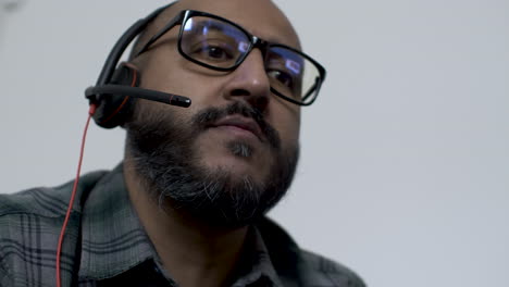 uk asian male talking on headset wearing glasses indoors working from home