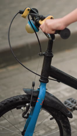 vista della gamba di un bambino che parcheggia una bicicletta nera su un sentiero asfaltato, il bambino tiene attentamente il manubrio mentre regola il supporto della bicicletta