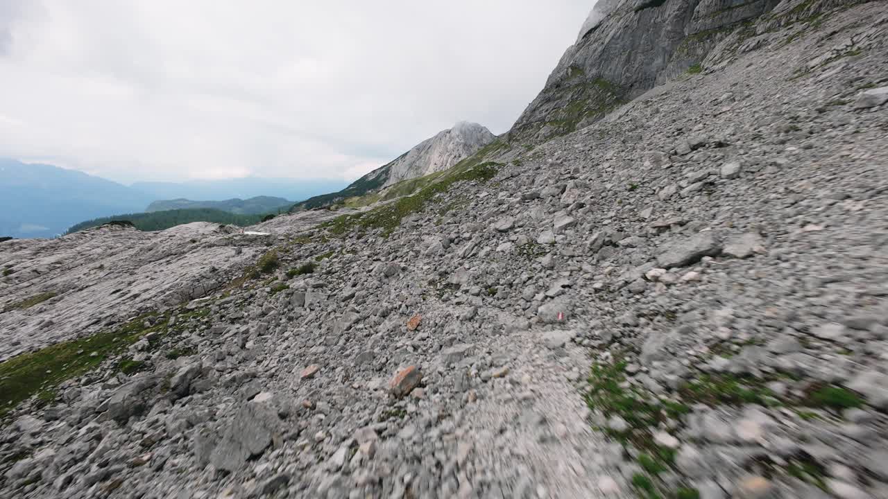 Drone flies low over rocky hiking trail in Tauplitz, Austria, with distant mountains in the background.