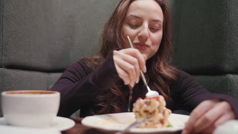 lady seated in green cafeteria booth smiles as she enjoys waffles with fork, savoring sweet treat beside cup of latte on wooden table, capturing cozy and cheerful breakfast moment in modern setting