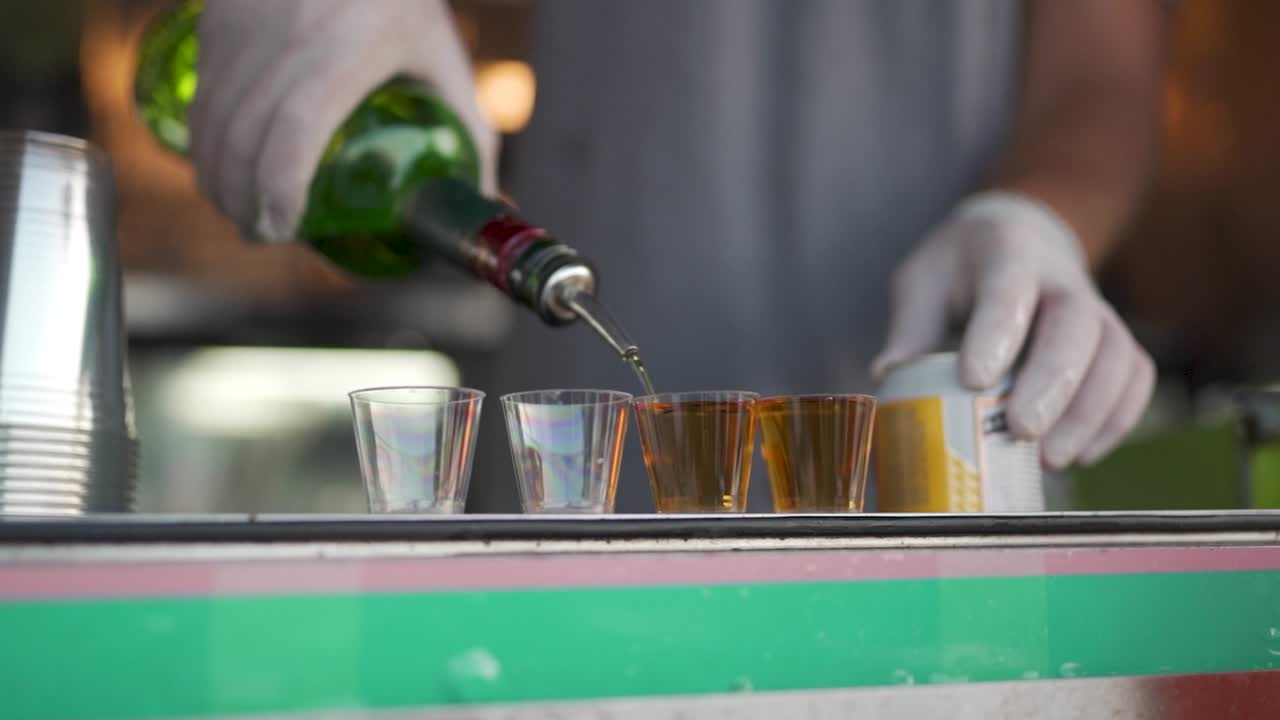 Close-up footage of a male bartender pouring shots at a cocktail party social.