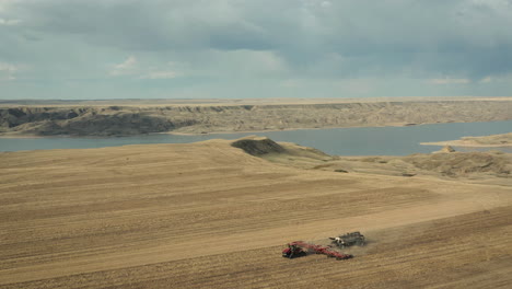 seeder machinery working on farmland with scenic river breaks as backdrop in saskatchewan, canada