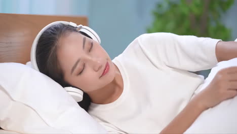 portrait active girl wearing pink headphones listening to music to sleep in bed room