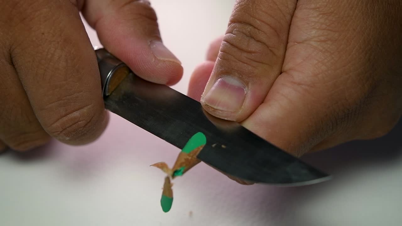 Filmato di mani che affilano lentamente una matita e alcune matite colorate con un coltello affilato.