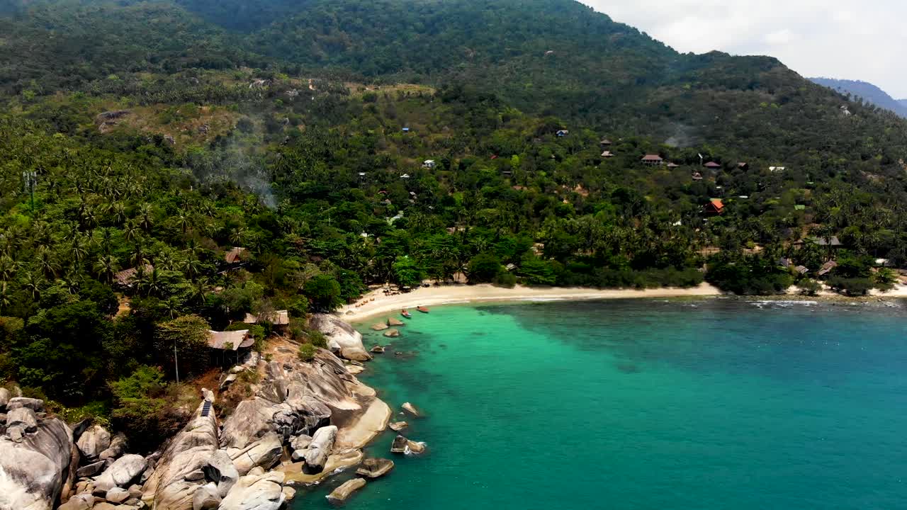 An overhead lifting aerial drone shot that reveals the huge boulders at the beach front of Haad Tian beach resort in Koh Tao island, Surat Thani province in Thailand