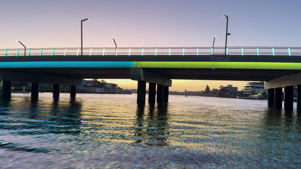 A serene boat journey under a bridge at sunset on Gold Coast, Australia. Calm waters and soft lighting create a tranquil atmosphere