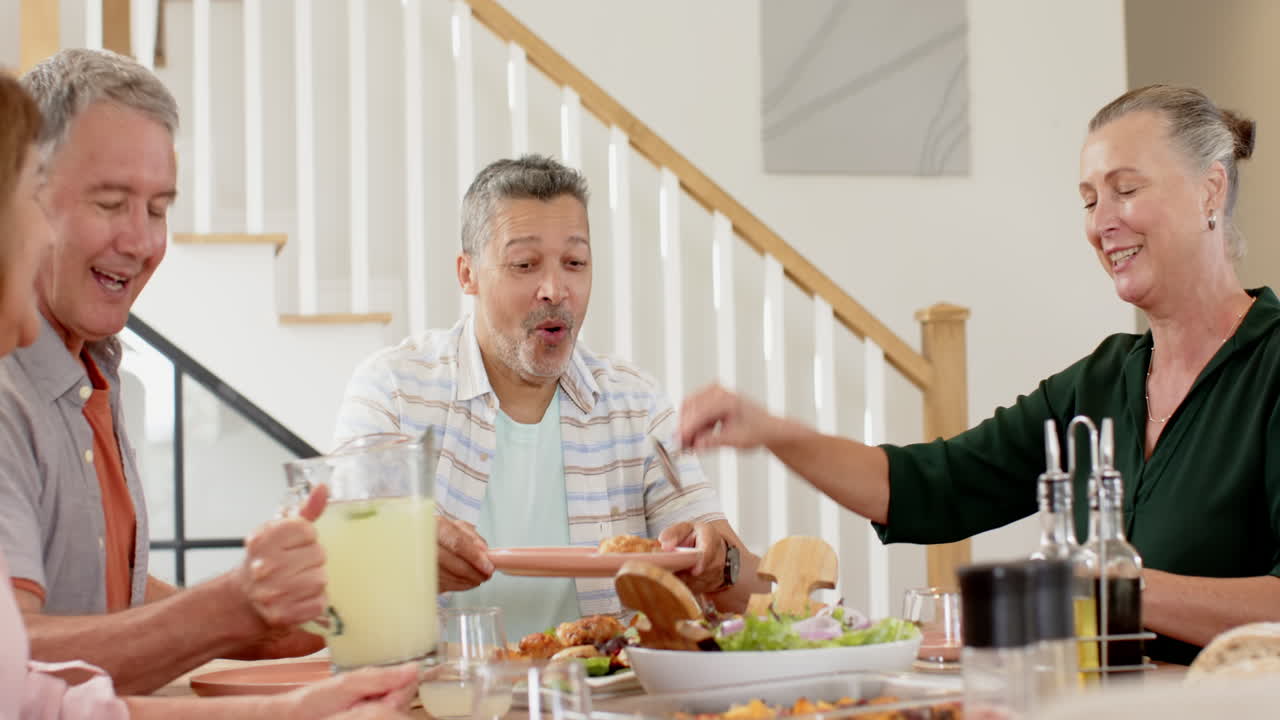 Enjoying meal together, senior friends laughing and sharing stories at dining table