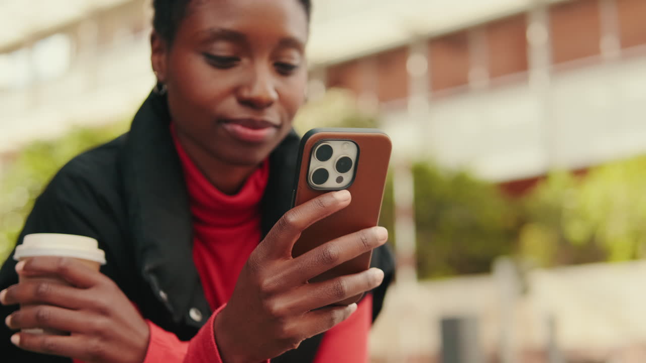 Giovane donna afroamericana che scorre lo smartphone e sorride all'aperto.