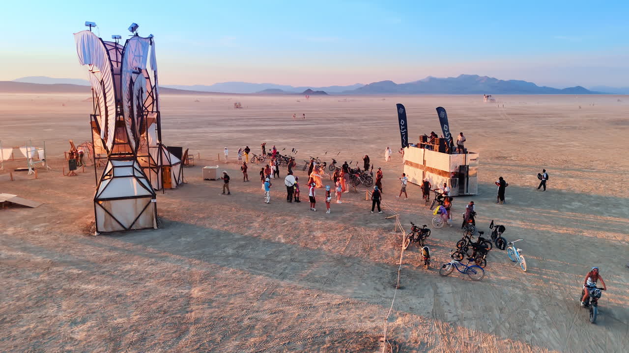 California, USA, 1 July 2025: Participants with bicycles near large white fabric sculpture. People gathered around a tall structure made of white fabric panels and a silver mobile unit in the desert