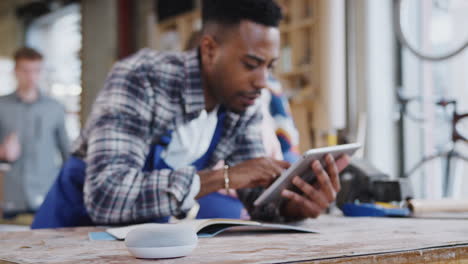 Male-Worker-In-Carpentry-Workshop-Using-Digital-Tablet-And-Asking-Smart-Speaker-Question