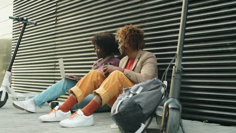 black man and woman sitting on street, using laptop and speaking