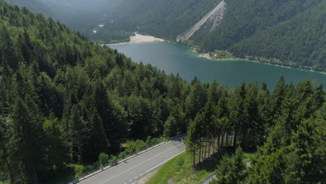 Drohnenschuss,-Der-über-Bäume-Auf-Einem-Berg-Neben-Einem-Von-Bergen-Umgebenen-See-Fliegt