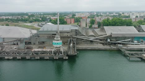 aerial establishing view of port cranes and empty loading docks at port of liepaja , liepaja city in the background, overcast summer day, wide drone dolly shot moving left