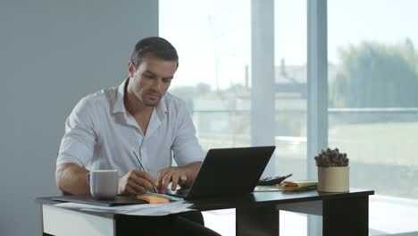 business man working at laptop computer. calm man making notes at workplace.