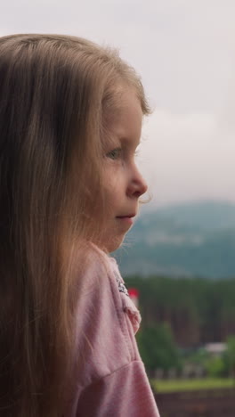 amazed long haired preschooler girl enjoys view of distant misty mountains from hotel room balcony at highland resort close view slow motion