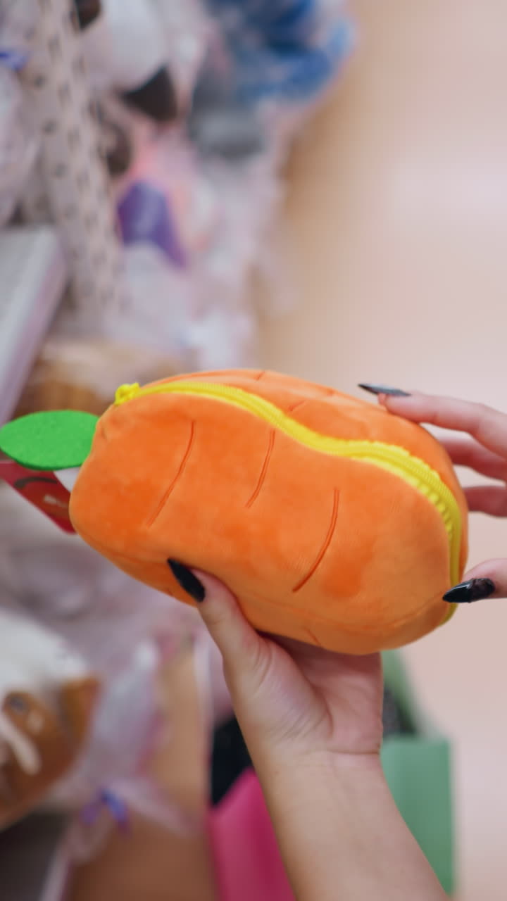 vista lateral de cerca de una mujer sosteniendo un elegante bolso de color naranja esponjoso con diseño de hoja verde, examinando detalles mientras hace compras, una compradora con uñas negras explora el pasillo de accesorios en una tienda minorista moderna