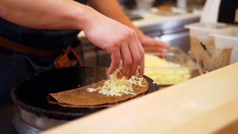 Chef-sprinkling-cheese-on-crepe