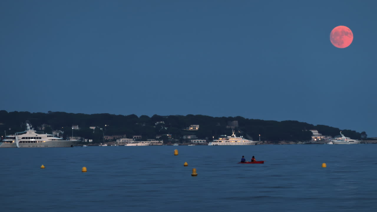 Boats on the sea in the evening with the moon up in the sky