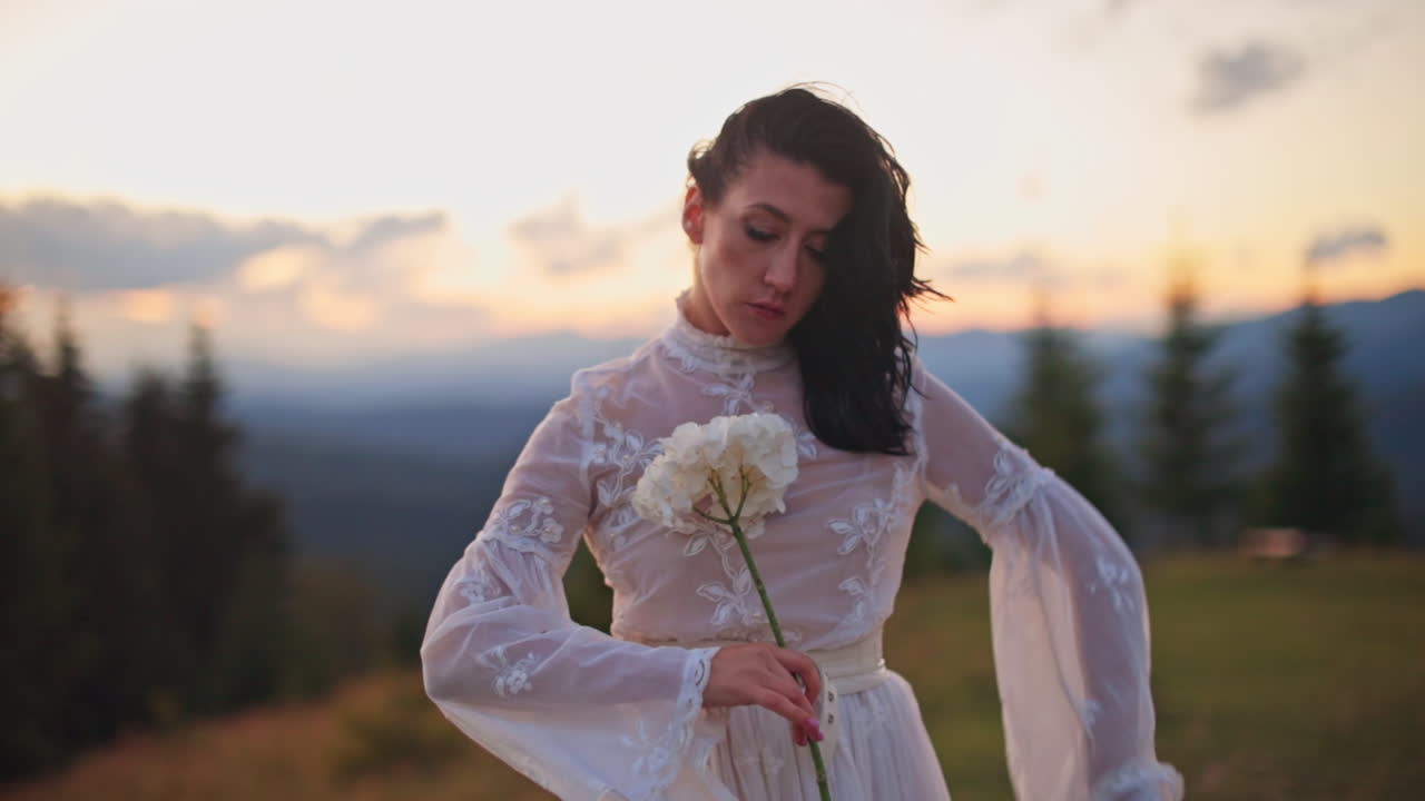 Donna in abito bianco con un fiore in mano al tramonto