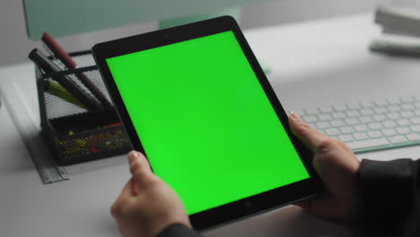 las manos sostienen la tableta verde en un primer plano contemporáneo en el lugar de trabajo.