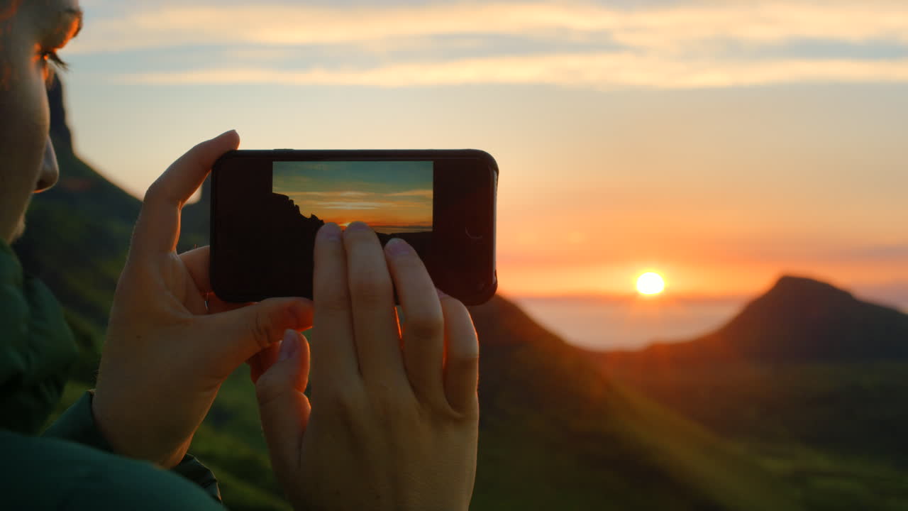 persona tomando una foto de una hermosa puesta de sol sobre las montañas
