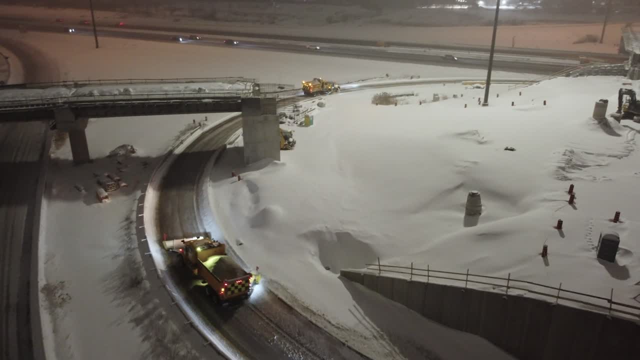 MISSISSAUGA, CANADA - FEBRUARY 15, 2025: Snow removal equipment clearing highway interchange during winter storm. Heavy machinery operates on curved ramps and bridges amid fresh snowfall.
